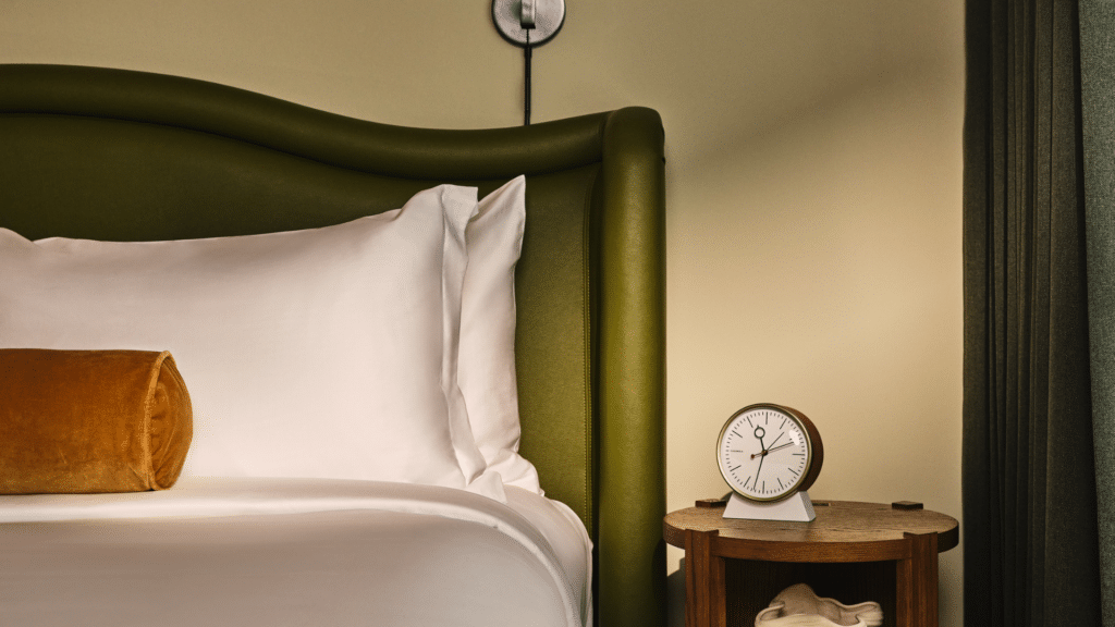 Bed with white linens, a green upholstered headboard, and a bedside table with a clock.