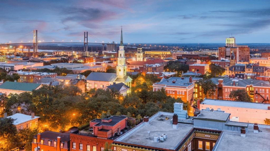 Elevated view of downtown Savannah’s rooftops, church steeples, and distant bridge at dusk.