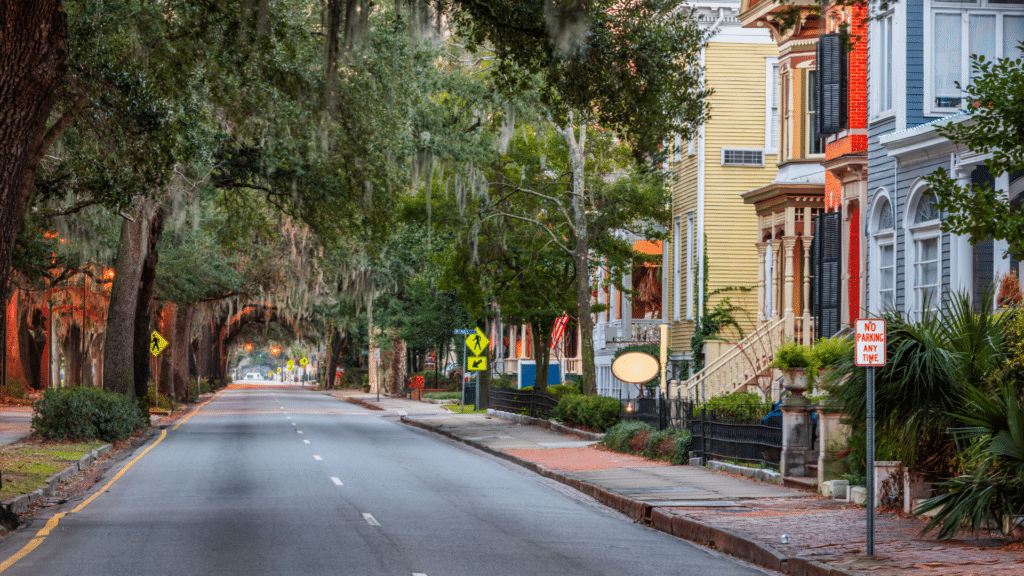 Colorful historic homes line a quiet Savannah street beneath moss-draped trees.