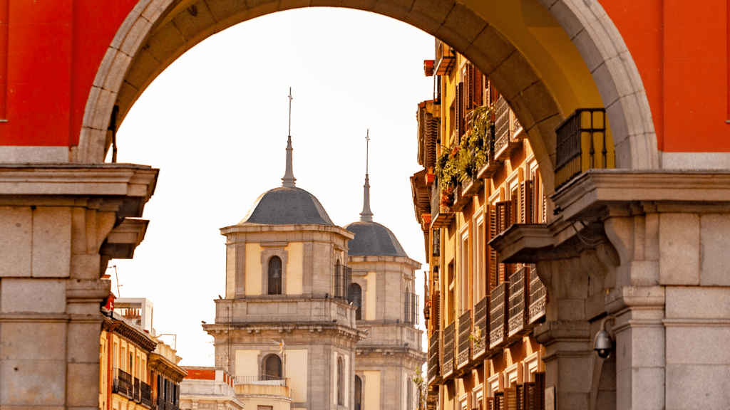 View through a stone arch toward a narrow Madrid street and twin church towers.