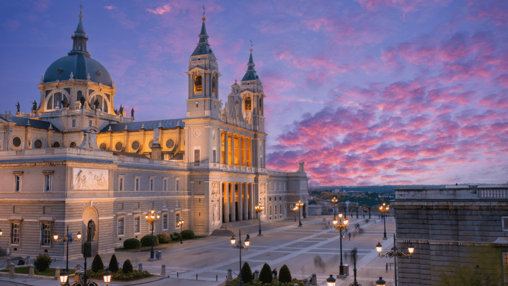 Almudena Cathedral’s dome and twin towers beneath a pink and purple evening sky.