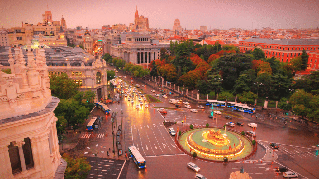 Elevated view of Madrid’s Plaza de Cibeles, illuminated fountain, and surrounding avenues at sunset.